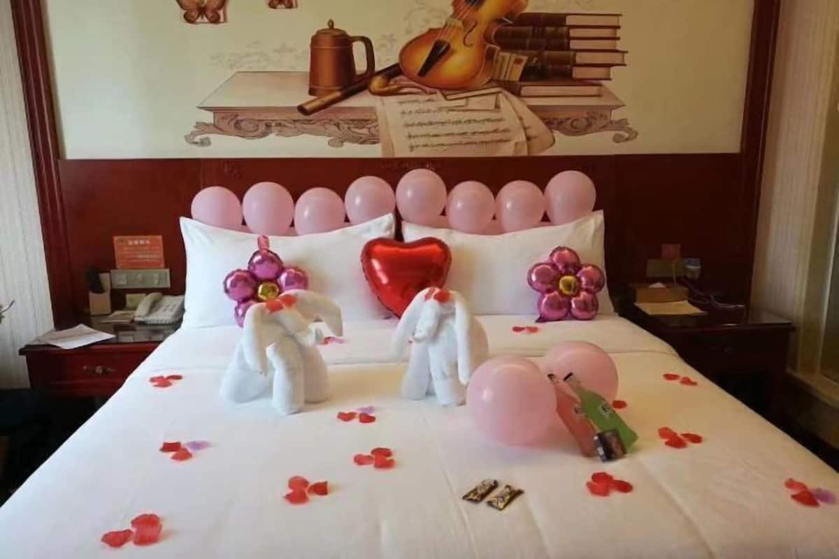 A hotel room with a neatly made bed, pink balloons, and stuffed animals.
