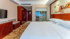 A hotel room with a large bed, a flat-screen TV, a wooden cabinet, and a painting on the wall. - Vienna Hotel (Ji'an Railway Station) (Ji'an)