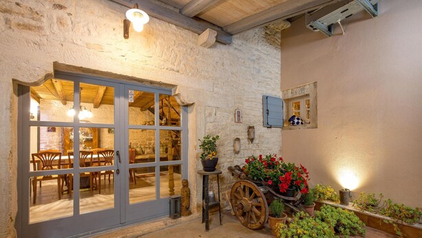 Un edificio rustico in pietra con interni in legno, un'ampia porta di legno e una carriola piena di fiori.