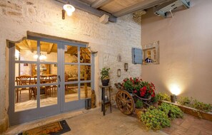 Un edificio rústico de piedra con interior de madera, una puerta de madera grande y una carretilla llena de flores.