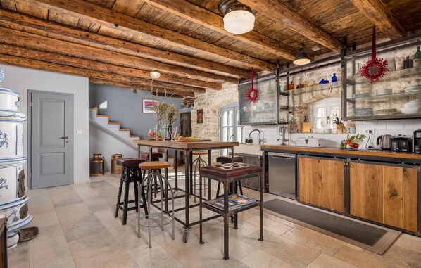 Una cocina rústica con vigas de madera a la vista, una isla central con taburetes y una pared de piedra.