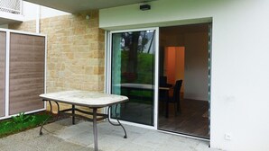 A patio area with a table and chairs, a sliding glass door leading to an interior room, and a brick wall. - Modern Apartment for 2-4, 400m from Beach, Terrace, Parking, Quiet Area (Sarzeau)