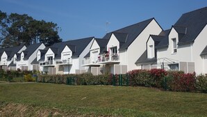 A row of white, two-story houses with dark roofs and balconies, surrounded by green hedges and a grassy lawn. - Modern Apartment for 2-4, 400m from Beach, Terrace, Parking, Quiet Area (Sarzeau)