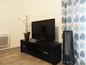 A black entertainment unit with a flat-screen TV, a potted plant, and a tall black lamp. - Modern Apartment for 2-4, 400m from Beach, Terrace, Parking, Quiet Area (Sarzeau)