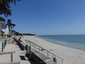 A beach with a concrete walkway, bicycles, and a clear blue sky.