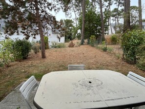 An outdoor patio with a concrete table and chairs, surrounded by trees and a grassy area. - Modern Apartment for 2-4, 400m from Beach, Terrace, Parking, Quiet Area (Sarzeau)