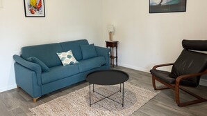 A living room with a blue sofa, a black chair, a small round table, and two framed pictures on the wall. - Modern Apartment for 2-4, 400m from Beach, Terrace, Parking, Quiet Area (Sarzeau)