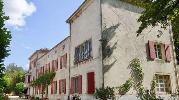 Un bâtiment historique avec des volets rouges, une cour pavée et des plantes en pot.