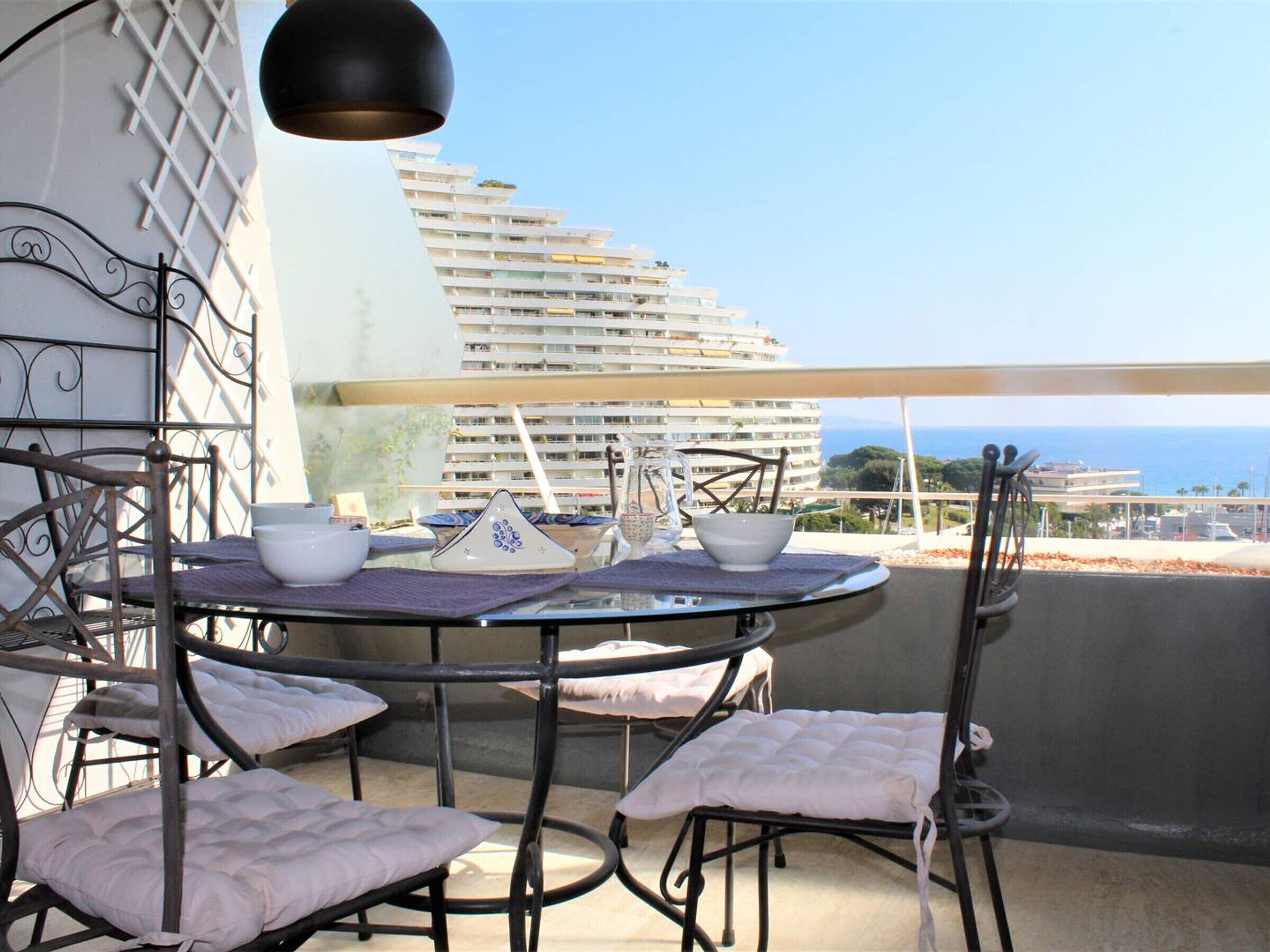 A balcony with a round table and four chairs, a hanging light fixture, and a view of a cruise ship and ocean.