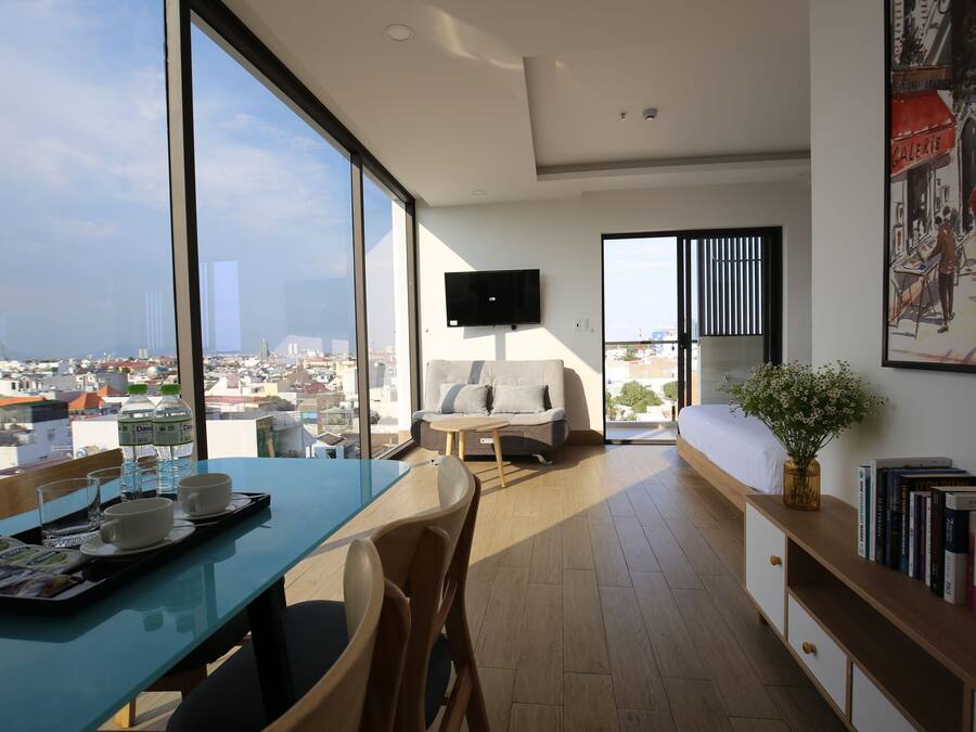 A modern living room with a large window, a sofa, a coffee table, and a TV mounted on the wall.