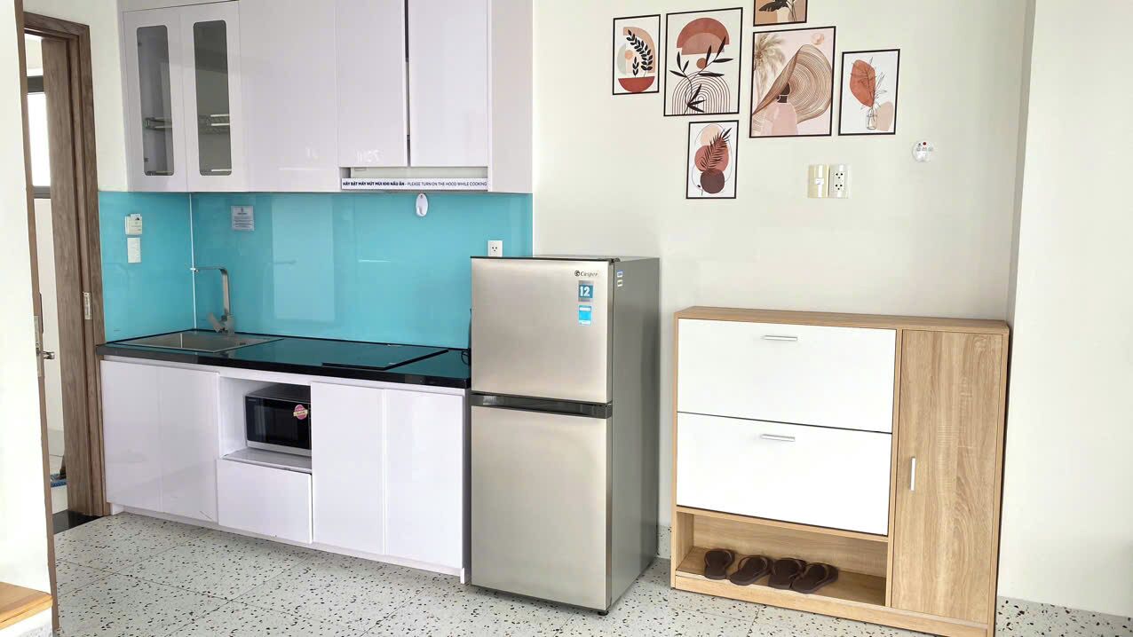 Una cucina compatta con mobili bianchi, un frigorifero in acciaio inossidabile, un forno a microonde e un armadietto con scarpe.