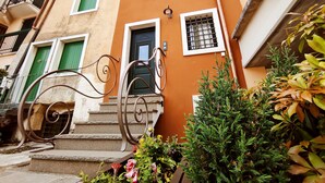 A multi-story building with a staircase leading to the entrance, a door with a metal gate, and a small garden area with plants. - BIG HOUSE, rent in mountain (Bosco Chiesanuova)