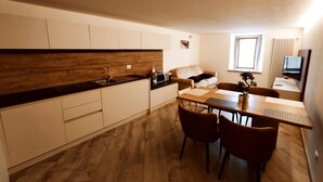 A modern kitchen with a wooden backsplash, a dining area with a table and chairs, a sofa, and a TV mounted on the wall. - BIG HOUSE, rent in mountain (Bosco Chiesanuova)