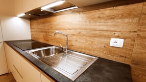 A modern kitchen with a stainless steel sink, wooden backsplash, and a black countertop. - BIG HOUSE, rent in mountain (Bosco Chiesanuova)