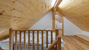Un plafond en bois à pente douce, un escalier en bois et un lit avec une literie à motifs.