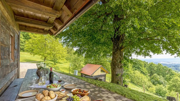 Un espace de restauration en plein air, avec une table dressée et garnie de plats et de boissons, entouré d’une végétation luxuriante et offrant une vue sur la campagne.
