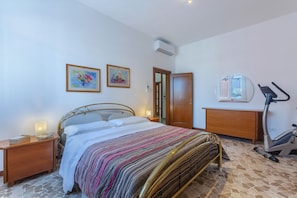 A bedroom with a bed, nightstand, exercise bike, and two framed artworks on the wall.