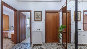 A hallway with a tiled floor, wooden doors, a white cabinet, and a framed picture on the wall.