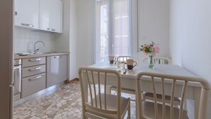 A kitchen with white cabinets, a tiled floor, a dining table with chairs, and a window with blinds.
