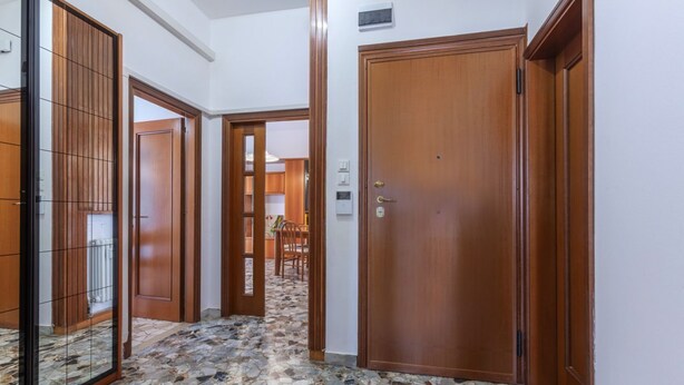 A hallway with a stone-tiled floor, wooden doors, and a view into a dining area.