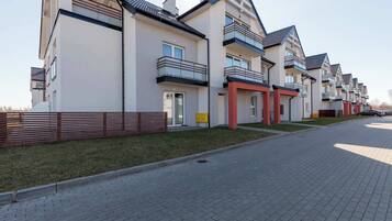 A row of modern apartment buildings with balconies, a paved driveway, and a wooden fence.