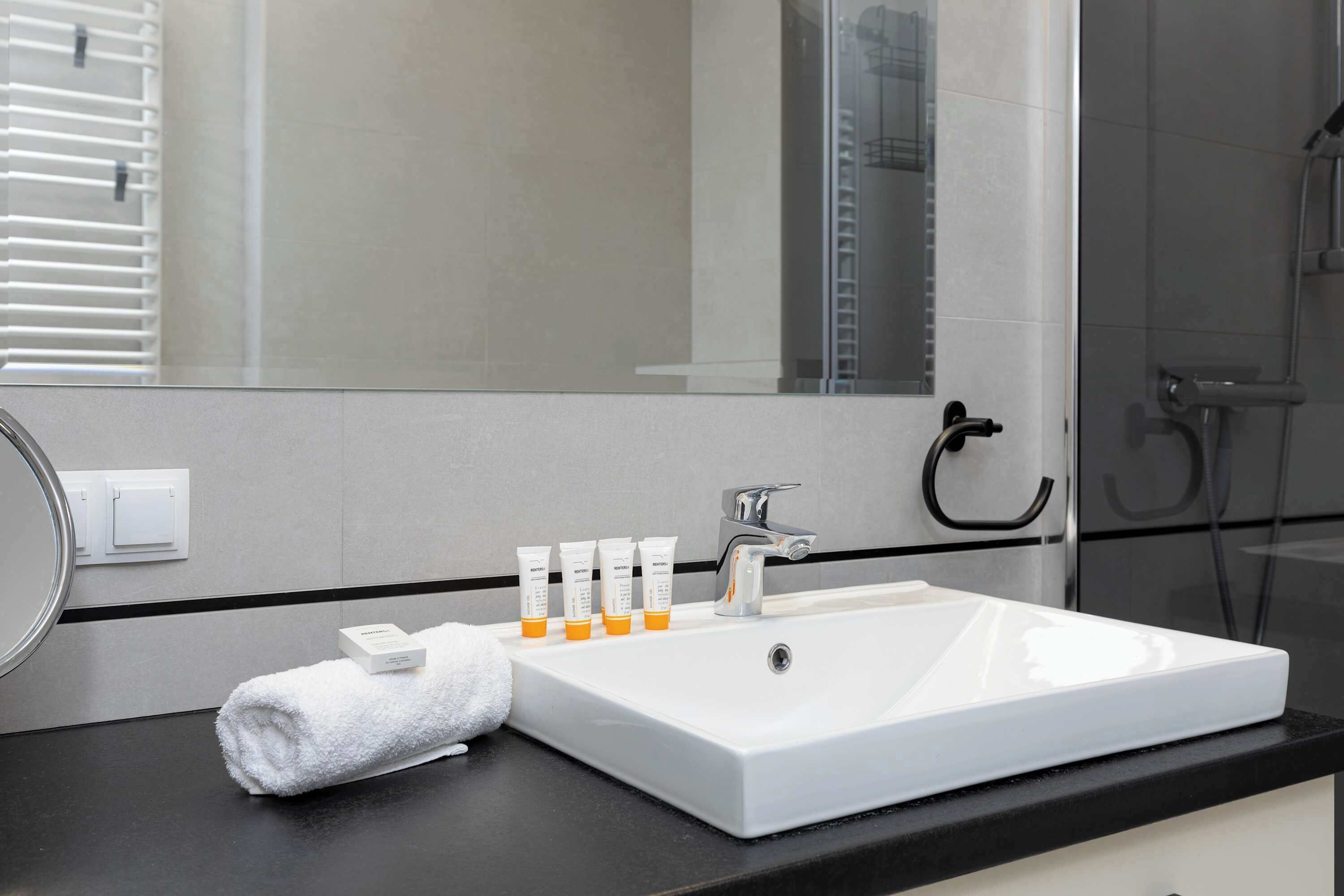 Un baño con lavamanos blanco, espejo y artículos de aseo.