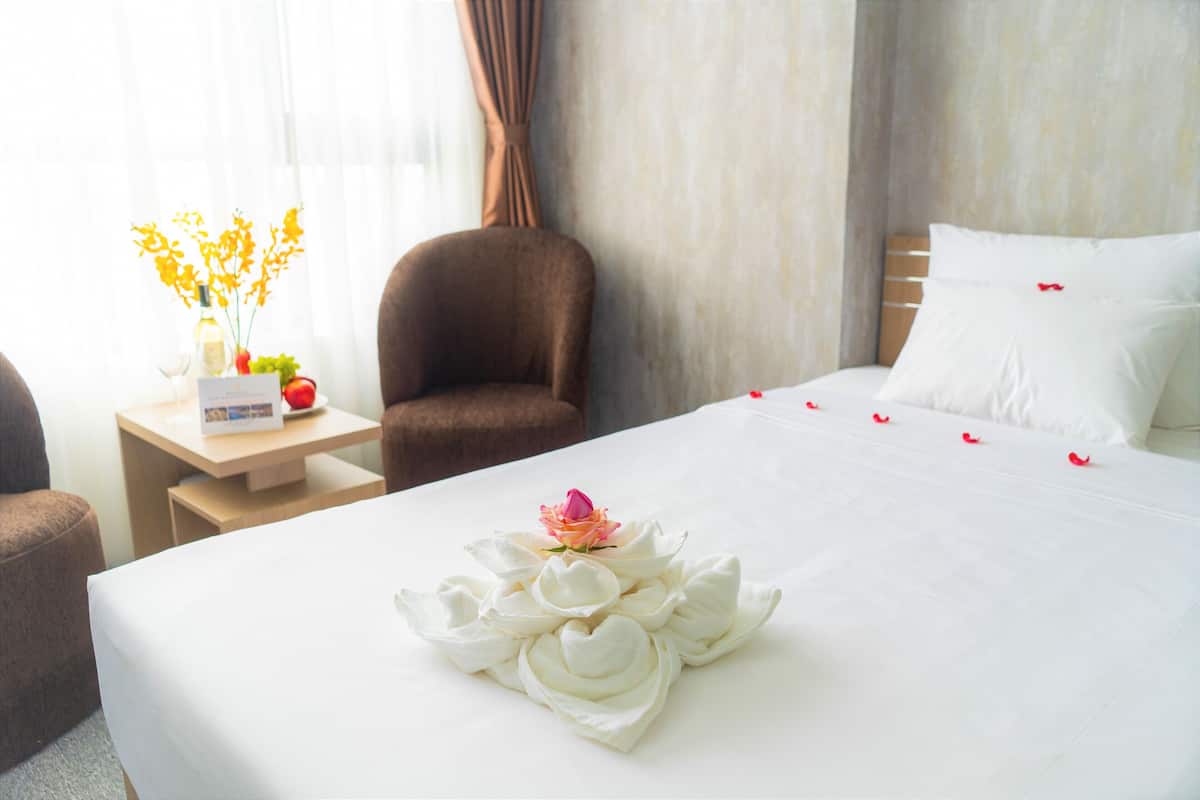 Una cama bien hecha con un arreglo floral, una mesita de noche de madera con un florero y un sillón marrón en una habitación de hotel.