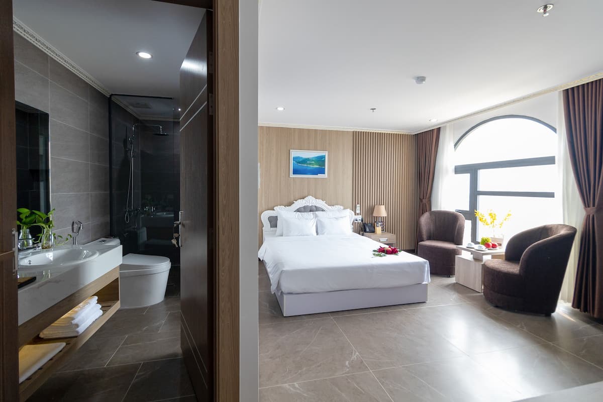 Una habitación de hotel con baño, cama, silla y ventana.