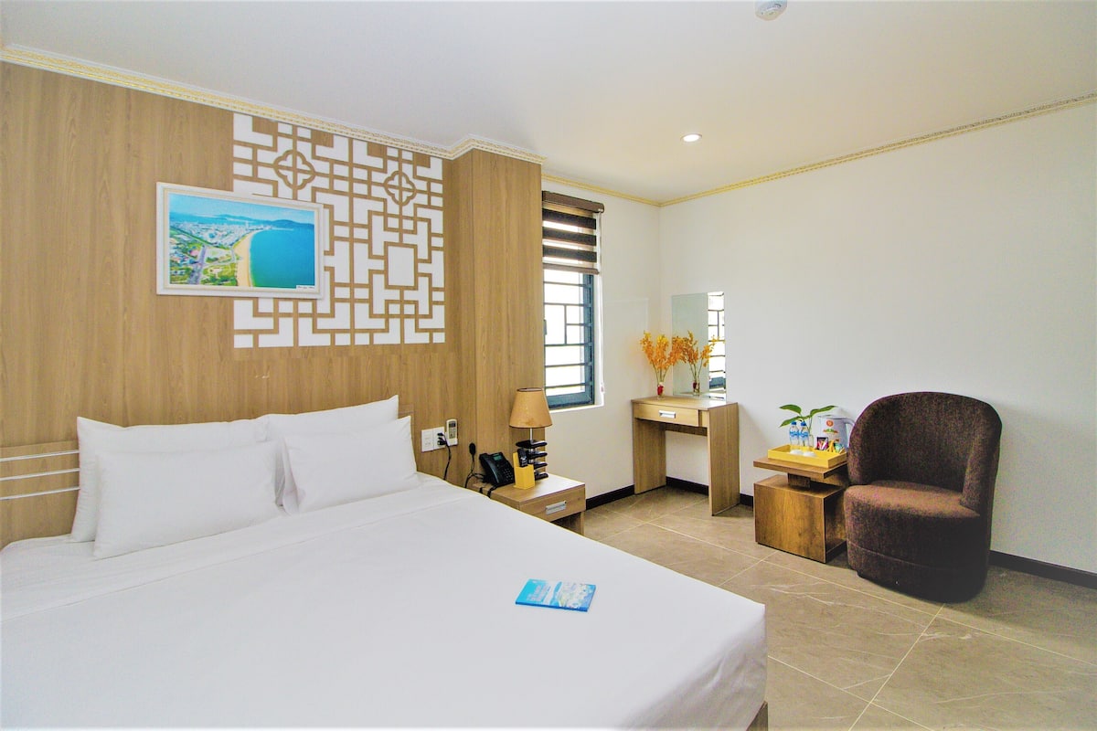 Habitación de hotel con cama, escritorio, silla, lámpara, teléfono y un panel decorativo en la pared.