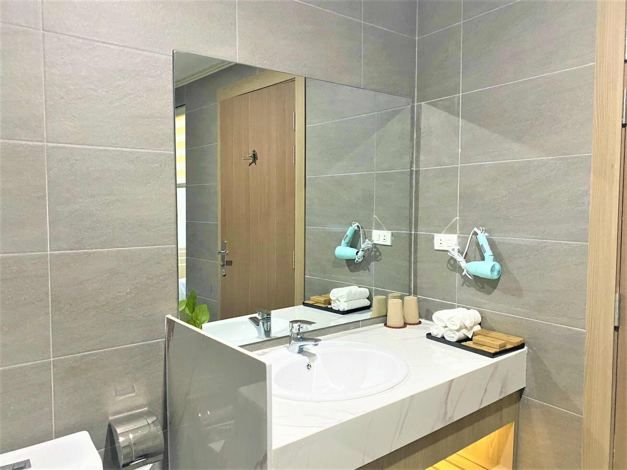 Une salle de bain moderne avec un grand miroir, un lavabo blanc et deux sèche-cheveux fixés au mur.