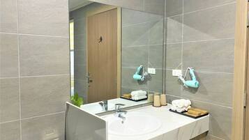 Une salle de bain moderne avec un grand miroir, un lavabo blanc et deux sèche-cheveux fixés au mur.