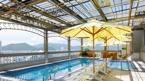 A rooftop pool with clear blue water, surrounded by white lounge chairs and yellow umbrellas, with a view of distant mountains. - Pearl Beach Hotel Quy Nhon (Quy Nhon Dong)