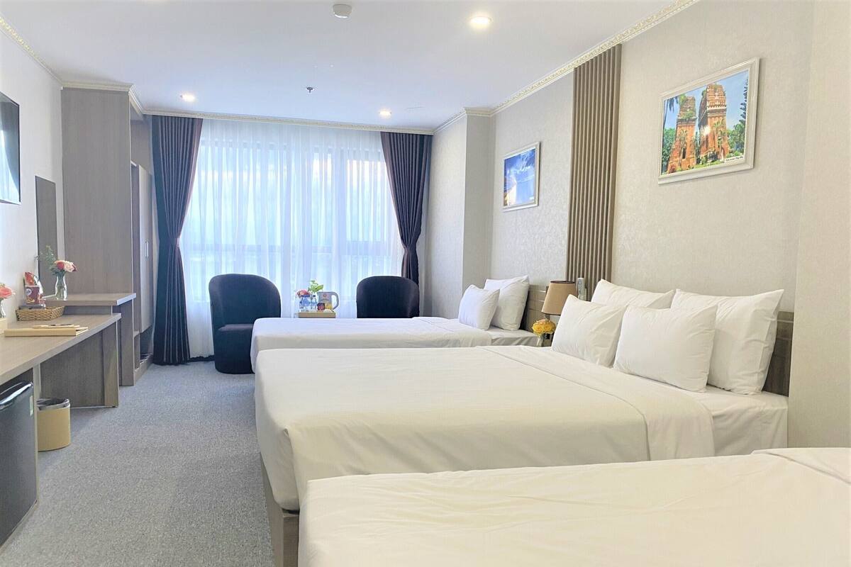 Habitación de hotel con dos camas, un escritorio, una silla, una mesita con una lámpara y un cuadro en la pared.