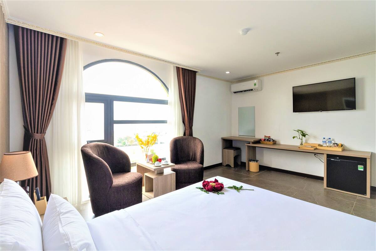 Habitación de hotel con cama, dos sillones, un escritorio con televisor y ventana con cortinas.