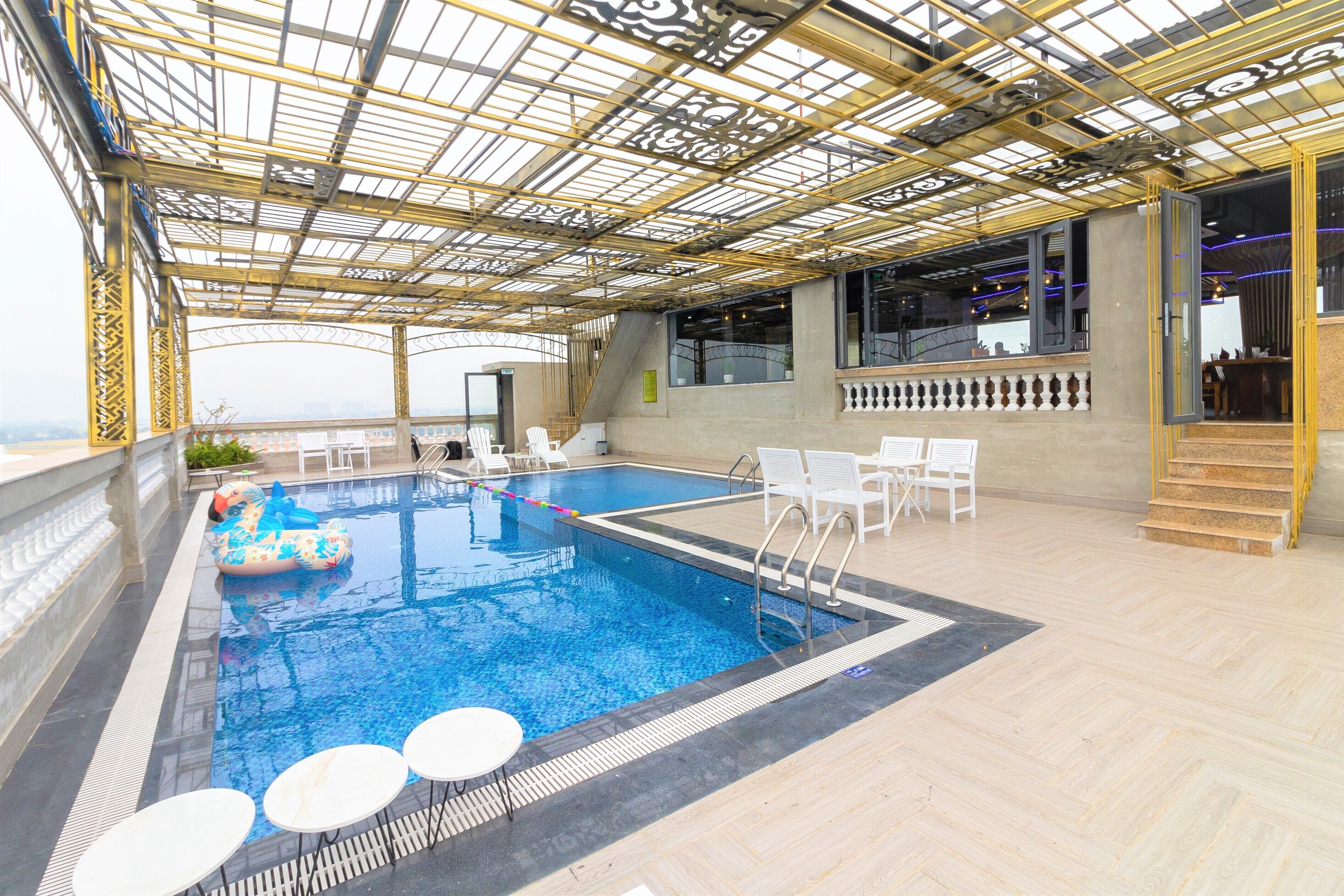 An indoor swimming pool with a glass ceiling, white lounge chairs, and a view of the city.