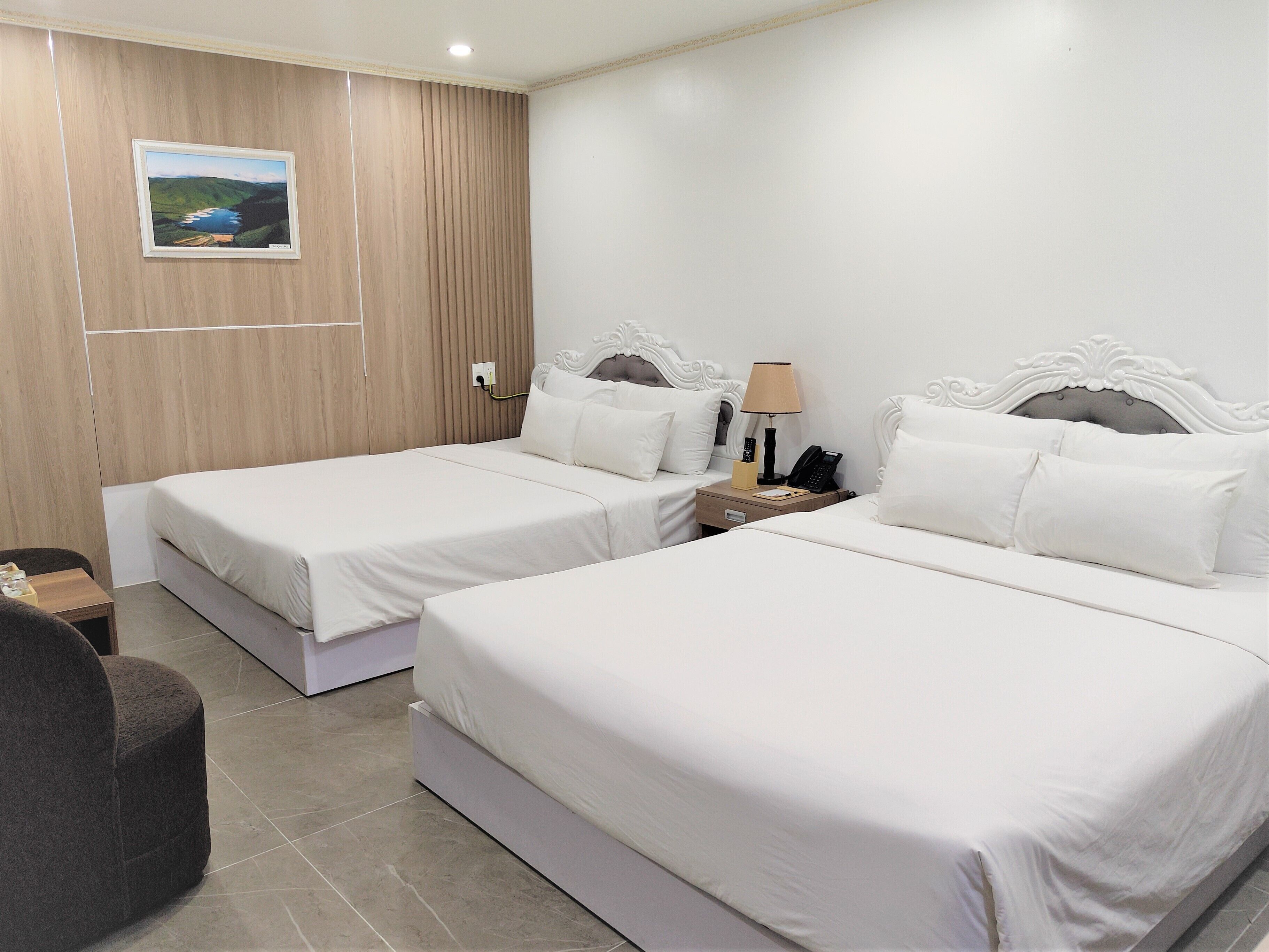 Une chambre d’hôtel avec deux lits, un mur recouvert de panneaux de bois, un tableau encadré, une table de chevet avec une lampe et un téléphone.