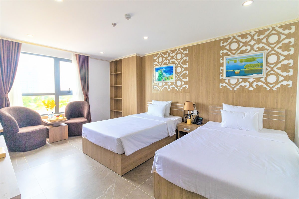 Habitación de hotel con dos camas, un escritorio, una silla y una ventana con cortinas.