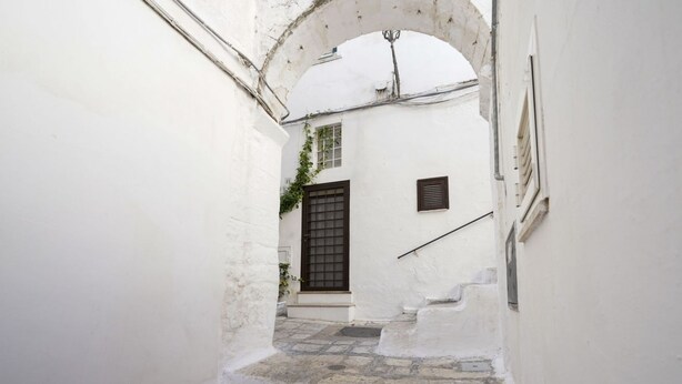 A narrow alleyway with a white building, a wooden door, and a small window.
