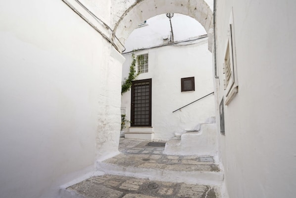 A narrow alleyway with a white building, a wooden door, and a small window.