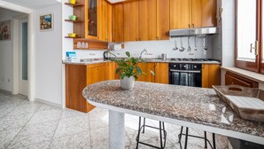 A modern kitchen with wooden cabinets, a granite countertop, a built-in oven, and a hanging pot rack. - ENEA - Sorrento Center with seaview (Sorrento)
