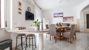 A modern kitchen with a marble countertop, bar stools, a dining table with chairs, a potted plant, and artwork on the walls. - ENEA - Sorrento Center with seaview (Sorrento)