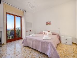A bedroom with a large sliding glass door leading to a balcony, a bed with pink bedding, a bedside table, and a wall-mounted light fixture.