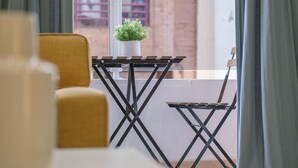 A balcony with a small table and chair, a potted plant, and a view of a building. - Bright, Clean & Very Comfortable Apartment (Valencia)