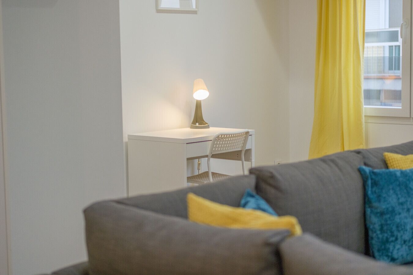 Een woonkamer met een bank, een bureau en een lamp.