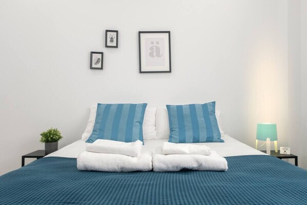 A neatly made bed with blue-striped pillows and a blue blanket, a small potted plant, and framed pictures on the wall.
