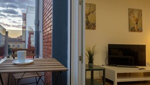 A balcony with a table, a chair, a potted plant, a TV, and artwork on the wall. - Bright, Clean & Very Comfortable Apartment (Valencia)