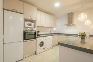A modern kitchen with a refrigerator, microwave, oven, washing machine, and a sink.