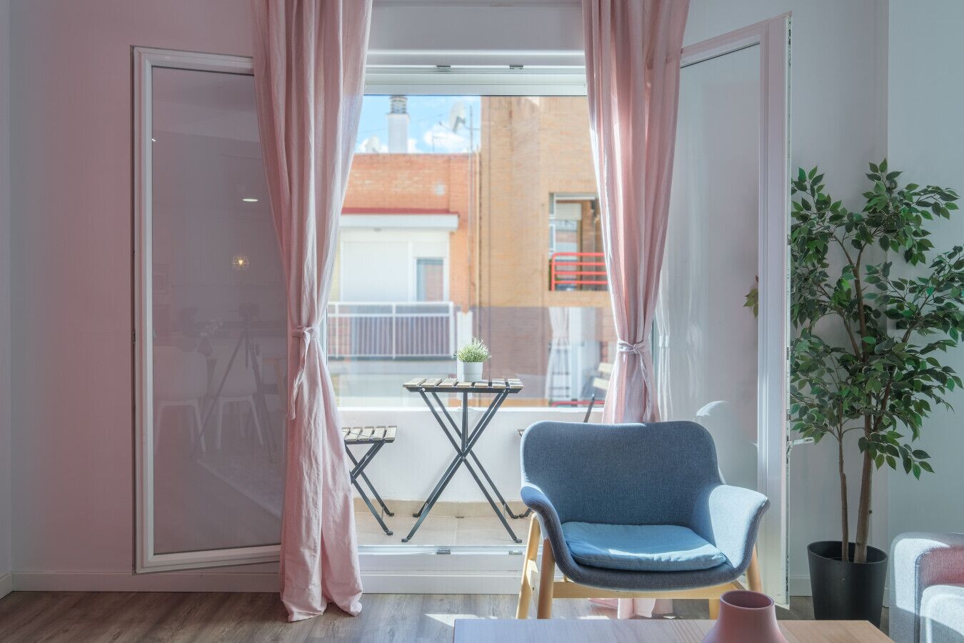 A room with a sliding glass door leading to a balcony, a blue chair, a small table, and a potted plant.