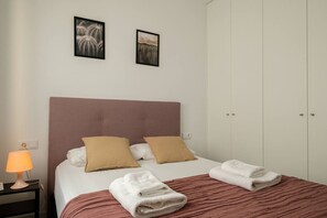 A neatly made bed with two pillows, a bedside table with a lamp, and a wardrobe.