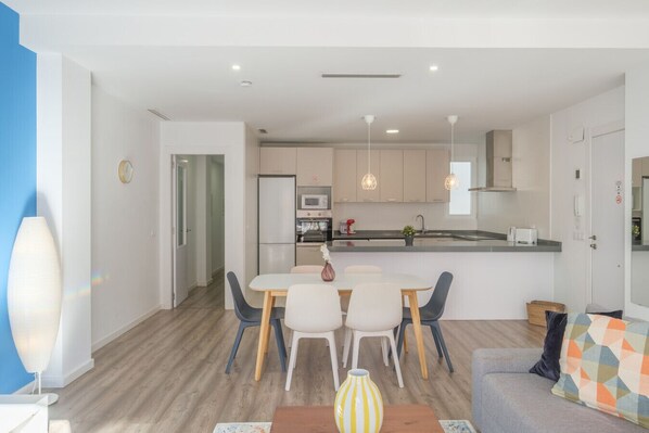 A modern kitchen with a central island, a dining area with a table and chairs, and a living area with a sofa and a patterned throw.